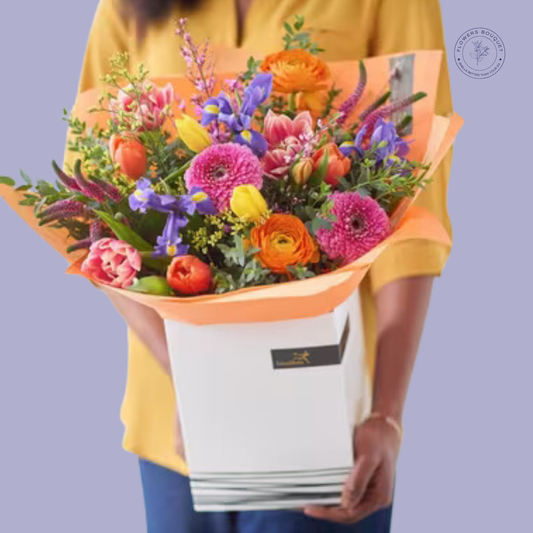 Bright spring bouquet with tulips, ranunculus, gerbera daisies, and iris, presented in a premium white gift box.