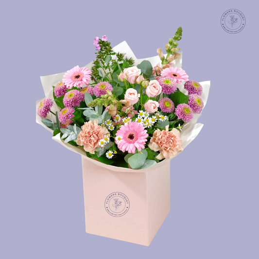 Spring Meadow Bouquet featuring pink gerbera daisies, spray roses, peach carnations, purple chrysanthemums, chamomile flowers, and eucalyptus in a pink gift box.